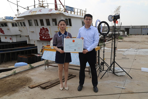 海鮮電商張夢(mèng)琴與幫辦員手持食品經(jīng)營(yíng)許可證合影。贛榆區(qū)委宣傳部供圖