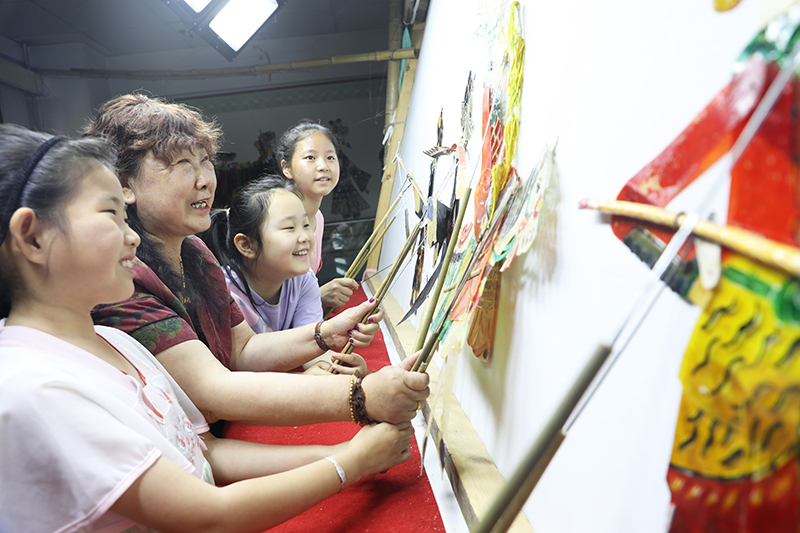 皮影藝人指導(dǎo)小朋友表演皮影戲。