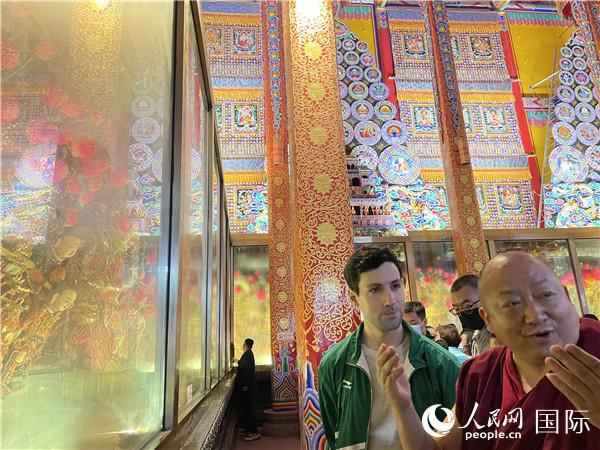 7月25日，省級非物質文化遺產項目塔爾寺酥油花的代表性傳承人朋措堅參（右）在塔爾寺酥油花館講解酥油花的制作過程。人民網 謝瑩攝