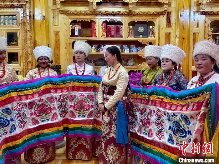 圖為女性展示村民自發(fā)繡制的“百米五彩哈達(dá)”?！±钣穹?攝